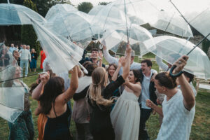 Mariés et invités sous la pluie avec des parapluies transparents